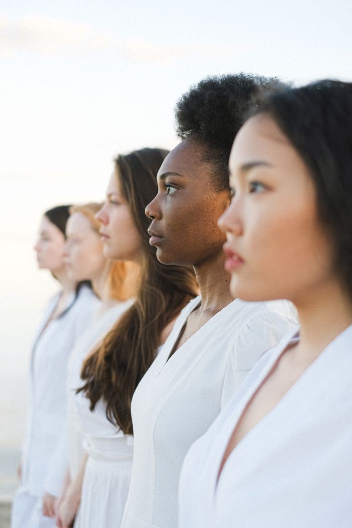 Five diverse women in white outfits standing side by side, symbolizing unity.